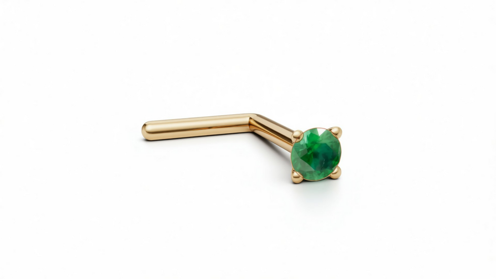 A gold-colored nose stud with a green gemstone is shown against a plain white background.