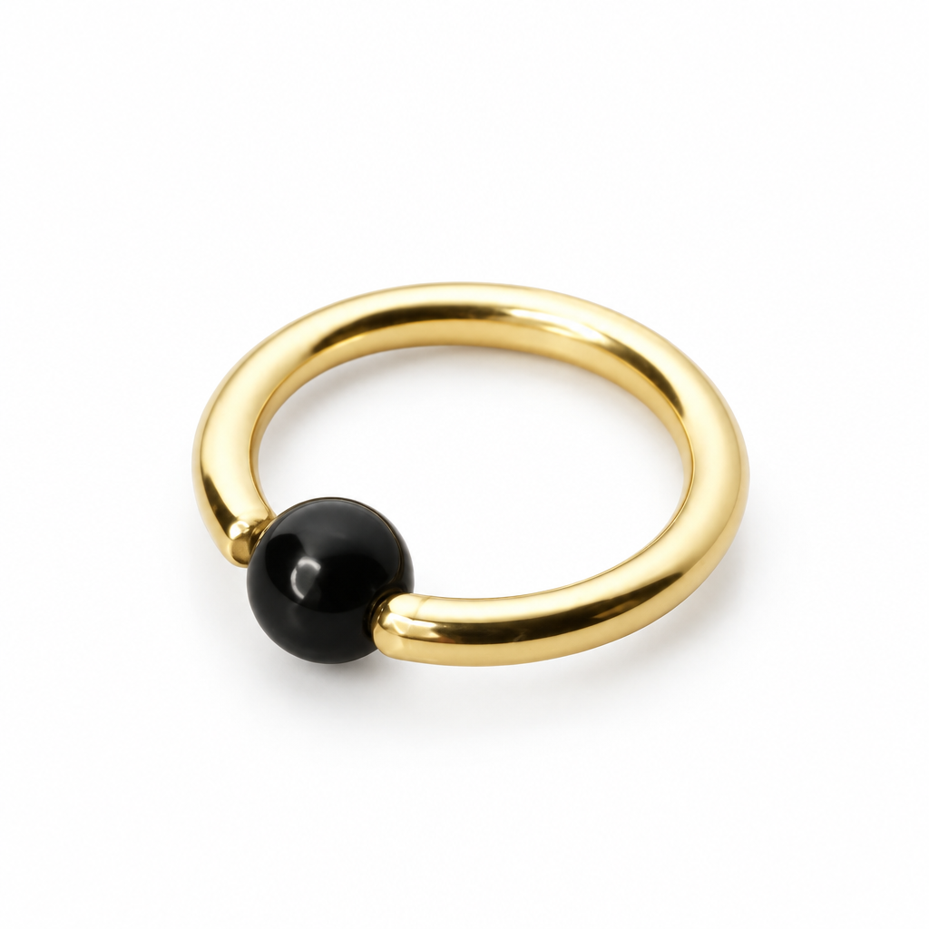 A minimalist gold ring with a smooth, polished black spherical bead set into the front, photographed on a clean white background.